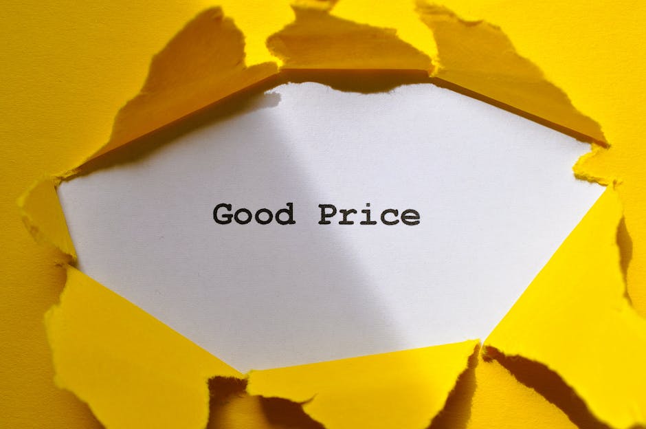 A white piece of paper with the words 'Good Price' typed in black font is visible through a torn section of a bright yellow paper or cardboard background. The torn edges around the opening are irregular and slightly frayed, revealing the smooth surface of the inner paper. The background appears to be part of a larger sheet or packaging material with a vivid yellow finish, creating a bold contrast with the white paper. This scene may relate to private or independent disposal options, such as discounted rubbish removal or clearance services, with the torn presentation suggesting a focus on uncovering value or affordability. The lighting is even, highlighting the texture of the torn edges and the crispness of the printed message, contributing to a clear and neutral observational style suitable for accessibility and SEO relevance in waste management contexts.
